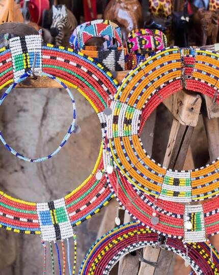 Colorful traditional beaded necklaces displayed on a wooden stand, showcasing vibrant African craftsmanship and cultural artistry
