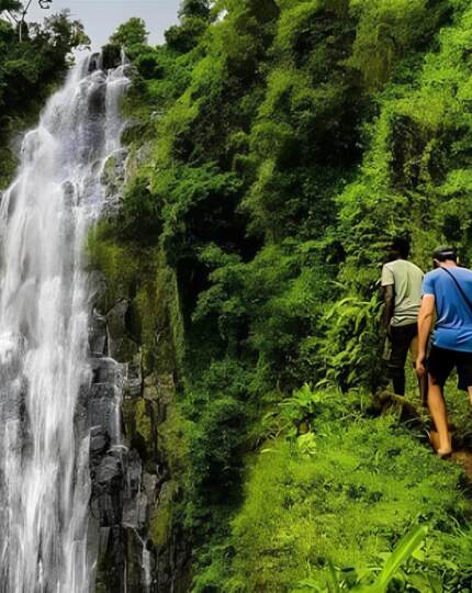 Group hiking barefoot along a lush green trail near a tall cascading waterfall surrounded by dense forest