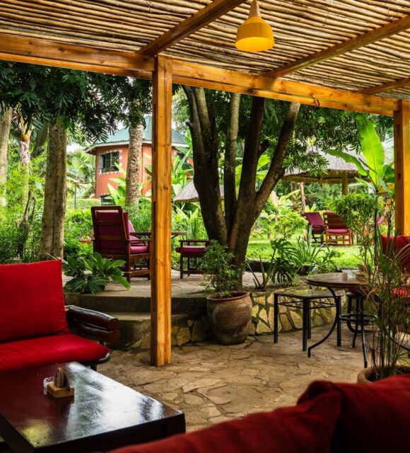 Outdoor lounge with red cushioned seating under a wooden pergola, surrounded by lush tropical garden and cozy seating areas