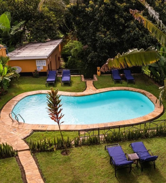 Cozy outdoor pool with stone deck surrounded by lush tropical plants and blue lounge chairs for guest relaxation