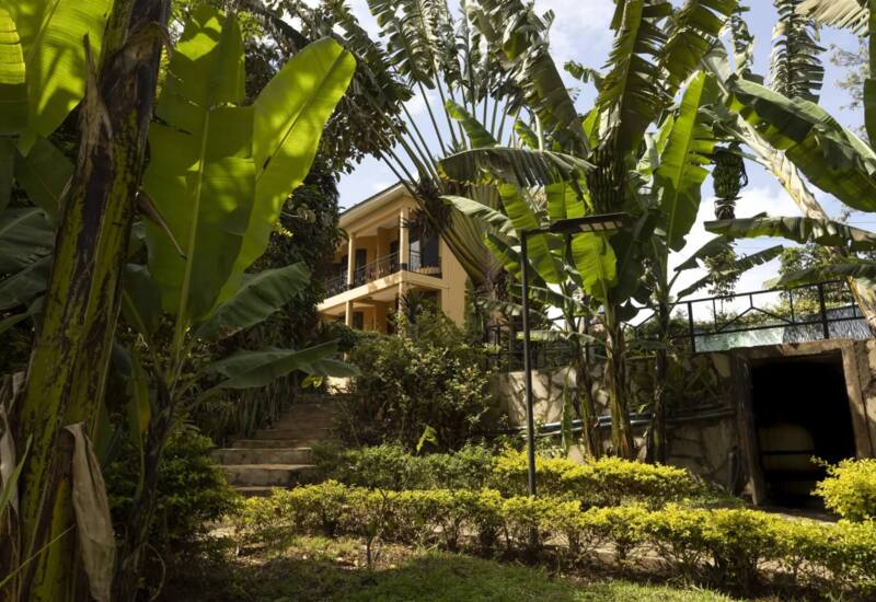 Two-story hotel building with balconies surrounded by lush tropical plants and banana trees under a bright sky