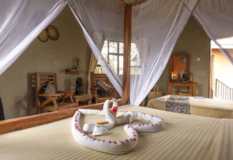 Cozy room with two beds featuring towel swans, wooden armchairs, decorative pillows, and soft natural lighting