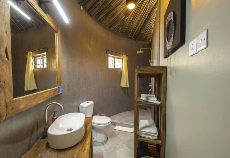 Rustic bathroom with wooden accents, vessel sink, walk-in shower, small window with yellow curtain, and neatly folded towels on wooden shelving