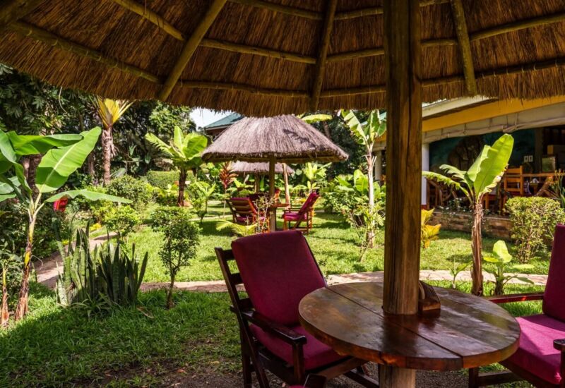 Shaded outdoor seating area with thatched umbrellas and red cushioned chairs surrounded by lush tropical garden at the hotel