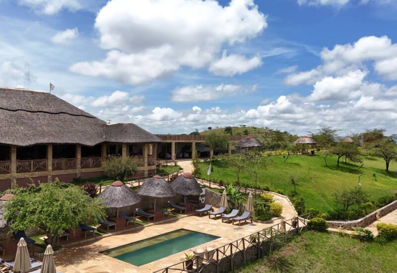 Lodge-style hotel with thatched roofs overlooking a small outdoor pool surrounded by sun loungers and umbrellas in a green hillside setting