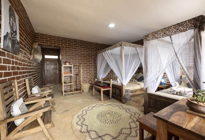 Rustic hotel room with twin canopy beds draped in white mosquito nets, wooden furniture, brick walls, and woven rug for a cozy ambiance
