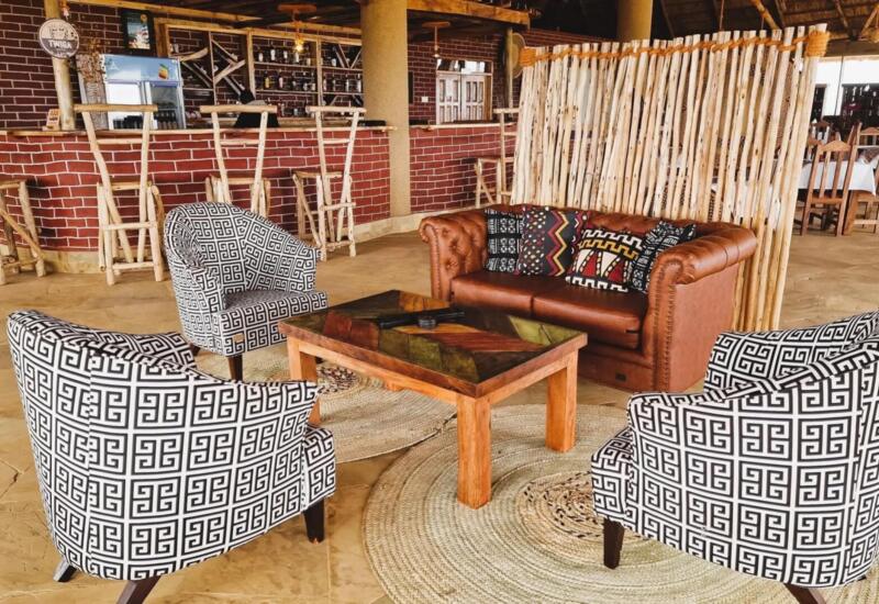 Cozy hotel lounge with patterned armchairs, leather sofa with vibrant pillows, rustic wooden coffee table, and a bar with natural wood stools