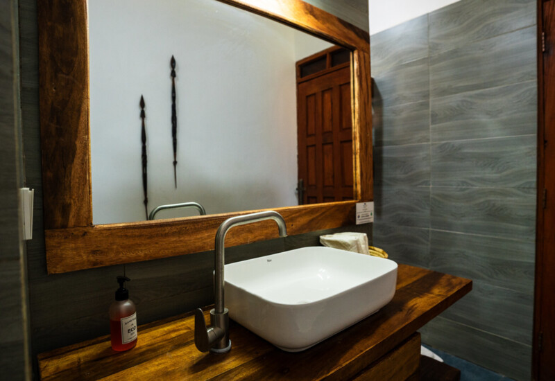 Modern bathroom with wooden countertop, white rectangular sink, stainless steel faucet, large wood-framed mirror, and gray tiled walls