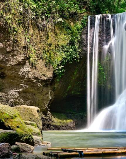 Secluded tropical waterfall cascading into a tranquil pool surrounded by moss-covered rocks and lush greenery