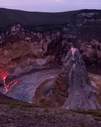 Dramatic volcanic crater with glowing red lava flows and rugged rocky formations at dusk, ideal for adventurous travelers.