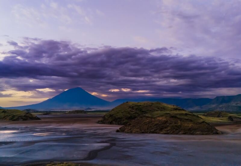 Expansive volcanic landscape at dusk with rugged hills and dramatic purple clouds under soft twilight