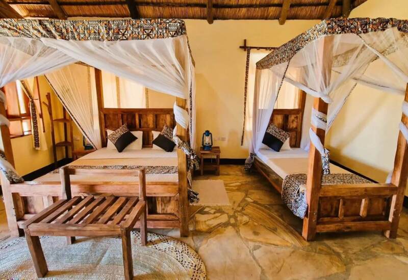 Cozy twin bedroom with wooden four-poster beds draped in patterned mosquito nets, rustic decor, and stone flooring