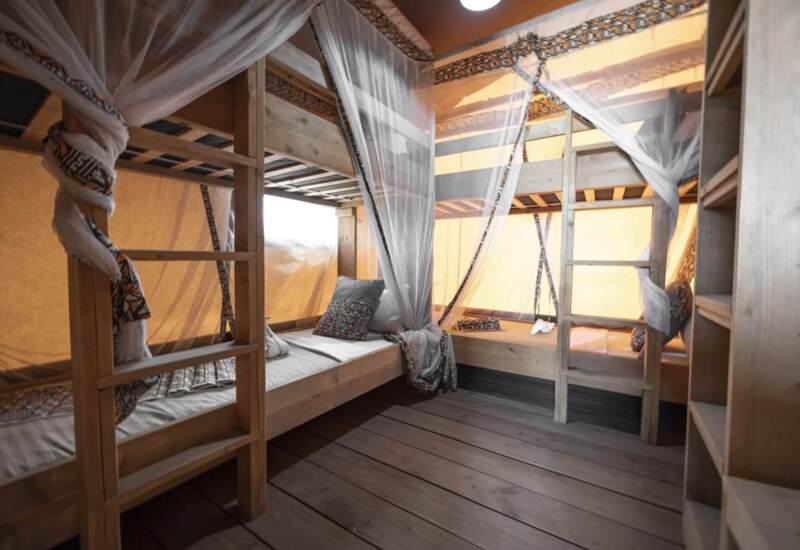 Cozy wooden bunk beds in a shared room with patterned pillows and sheer white mosquito nets in a rustic lodge or glamping tent
