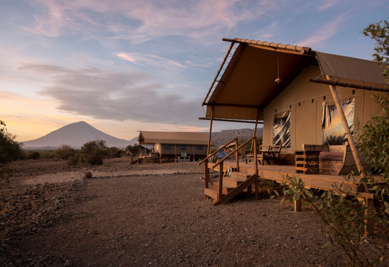 Luxury safari tents with wooden decks and seating, set in a serene landscape with a mountain view at sunset