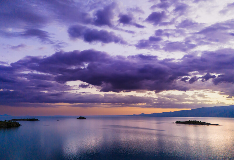Calm coastal view at twilight with small islands, a smooth sea reflecting purple clouds, and distant mountain silhouettes