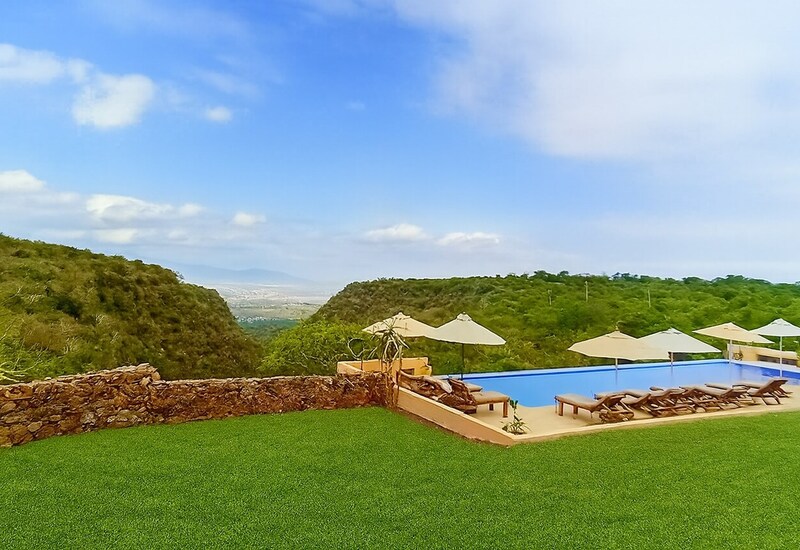 Infinity pool with sun loungers and umbrellas on a hillside terrace overlooking a green valley and distant mountains.
