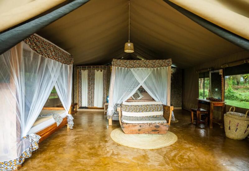 Luxury safari tent with two canopy beds draped in mosquito nets, African-print textiles, wooden seating and verdant views.