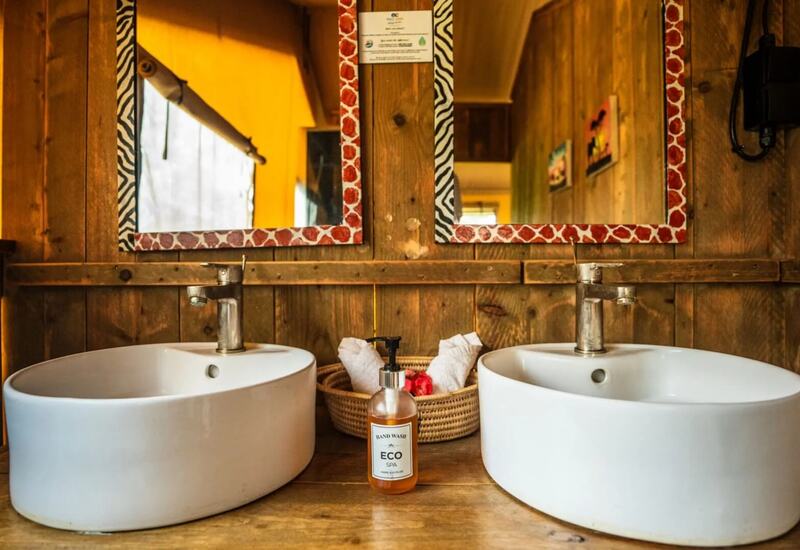 Rustic bathroom vanity with two white vessel sinks, patterned mirrors, wicker basket with rolled towels, Eco Spa hand wash.