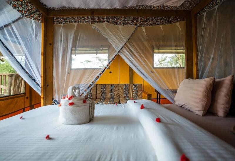Safari-style tent suite with four-poster bed draped in mosquito netting, towel swan with rose petals, patterned cushions and private wooden deck.