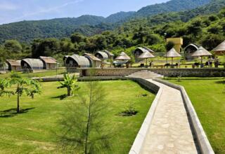 Eco-friendly tents and stone cottages set in lush greenery with hills in the background, featuring shaded lounge areas and walking paths