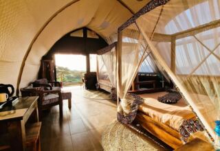 Luxury glamping tent with queen canopy bed, patterned upholstery chairs, wooden furniture, and scenic view from balcony
