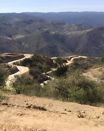 Winding dirt road cuts through arid mountain landscape with sparse vegetation under clear blue sky