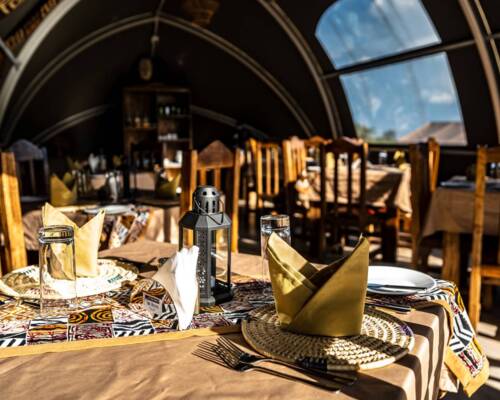 Cozy dining area with rustic wooden chairs and tables set with woven placemats, folded napkins, and decorative lanterns inside arched windows