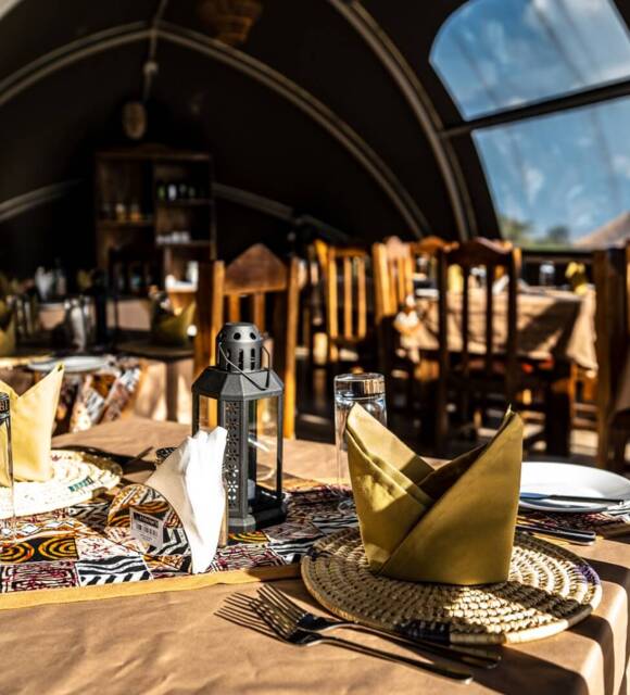Cozy dining area with rustic wooden chairs and tables set with woven placemats, folded napkins, and decorative lanterns inside arched windows