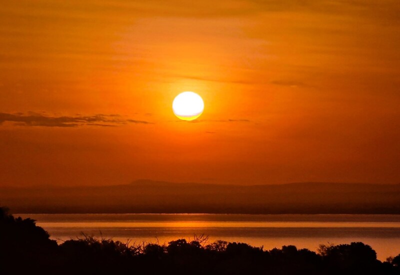 Golden sunset over calm water with silhouetted trees and distant hills, creating a peaceful natural view