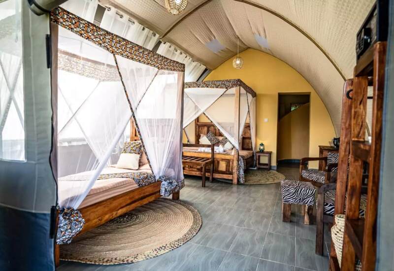 Spacious tented room with two wooden canopy beds draped in white mosquito nets, patterned cushions, and cozy seating area