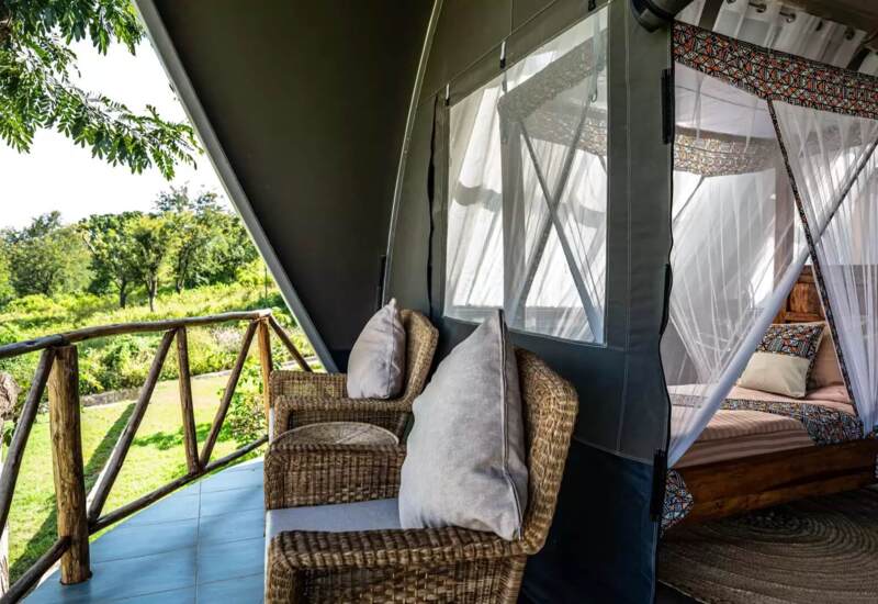 Outdoor terrace with woven armchairs and cushions, overlooking lush greenery; inside, a cozy bed with patterned mosquito netting.
