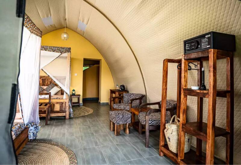 Cozy glamping tent interior with curved quilted walls, wooden furniture, zebra-patterned chairs, and a secure safe on a shelf