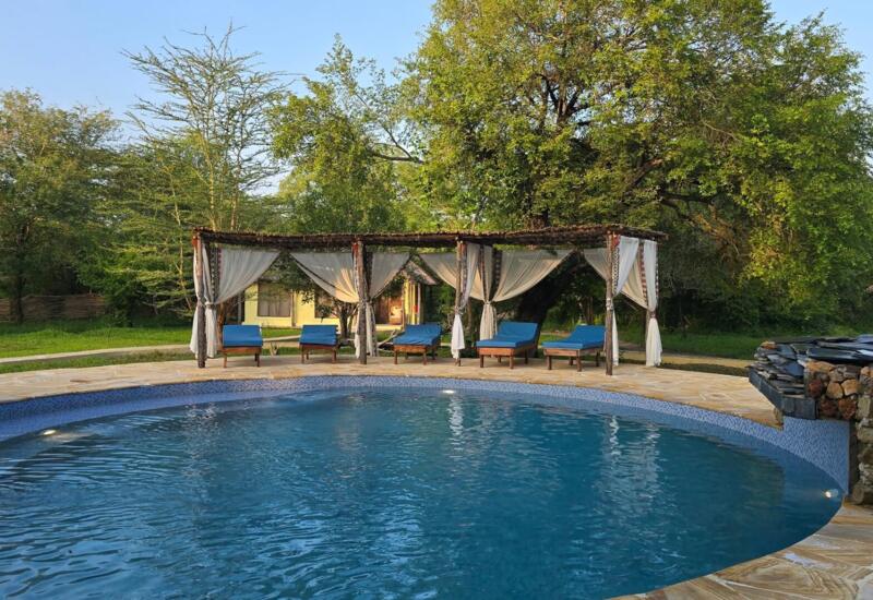 Tranquil outdoor pool with blue loungers under wooden pergolas draped with white curtains, surrounded by lush greenery