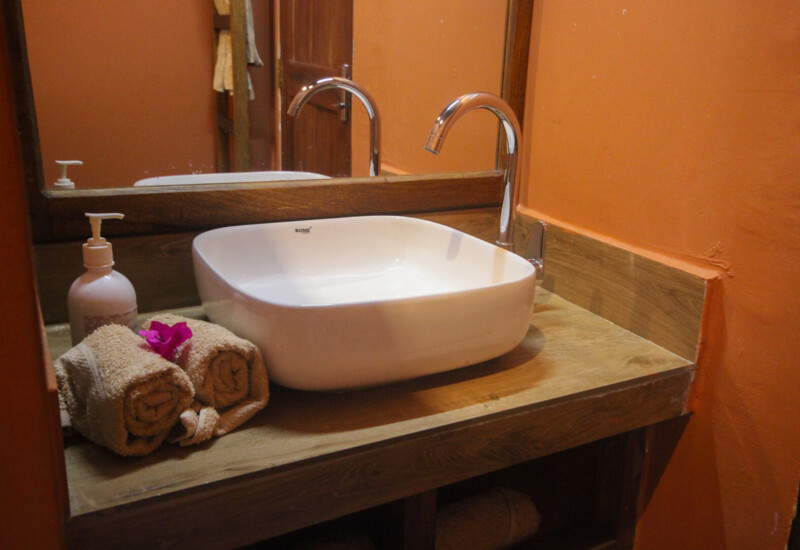 Hotel bathroom with a modern white square sink, chrome faucet, wooden countertop, beige towels, and orange walls