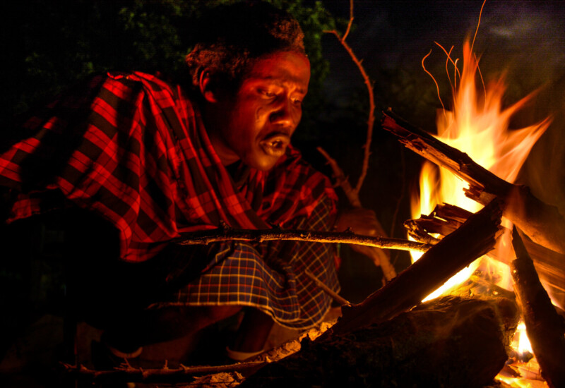 Person in traditional attire tending a campfire outdoors at night, creating a warm and rustic ambiance.