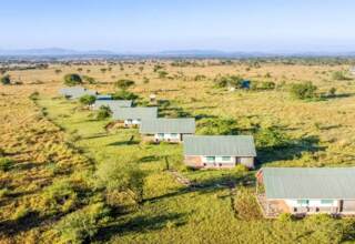 Row of private stone cottages with green roofs set in a vast savanna landscape with distant mountains under a clear sky