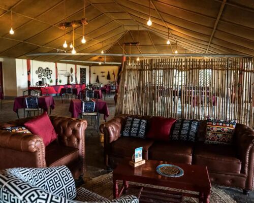 Cozy lounge area with leather sofas, patterned cushions, and a rustic dining room featuring tables with maroon tablecloths and eclectic decor