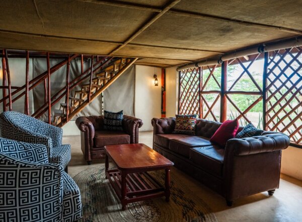 Cozy lounge area with leather sofas, patterned armchairs, wooden coffee table, and rustic lattice windows overlooking greenery
