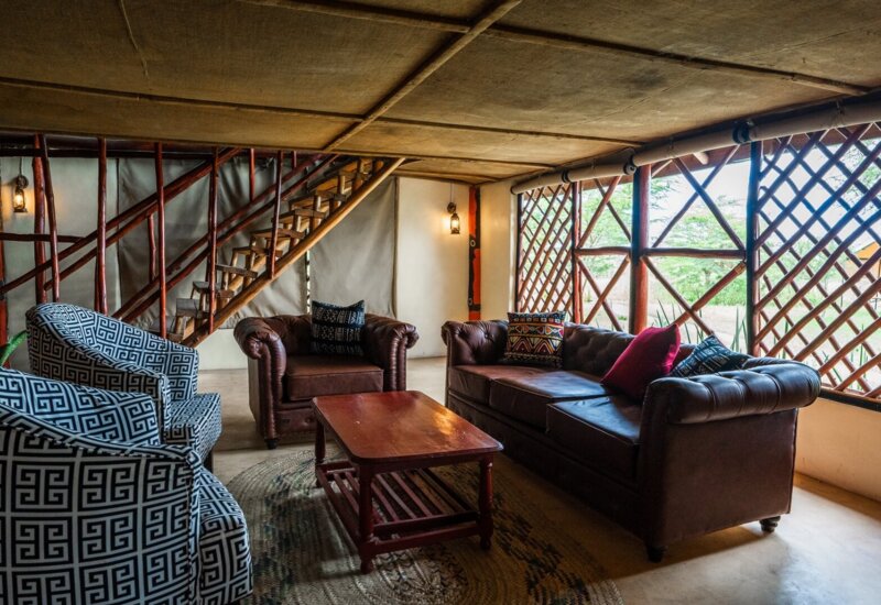 Cozy lounge area with leather sofas, patterned armchairs, wooden coffee table, and rustic lattice windows overlooking greenery