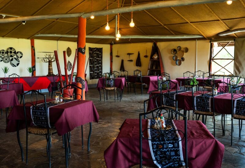 Cozy tribal-themed restaurant with maroon tablecloths, black wrought-iron chairs, earthy decor, and warm ambient lighting