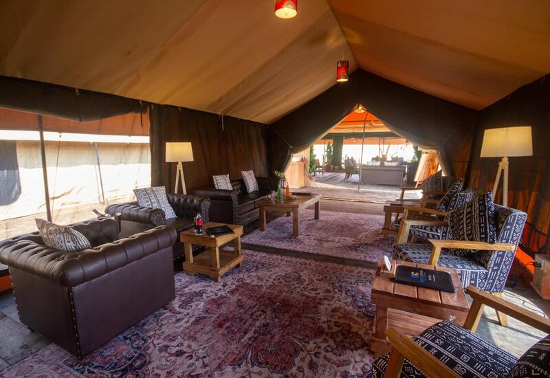 Luxury safari tent lounge with leather chesterfield sofas, patterned wooden armchairs, rustic coffee tables and warm lamps.