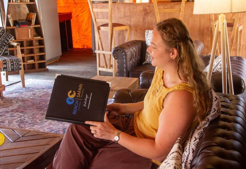Guest relaxing in cozy safari lounge on leather sofa, holding a Beach Safari brochure