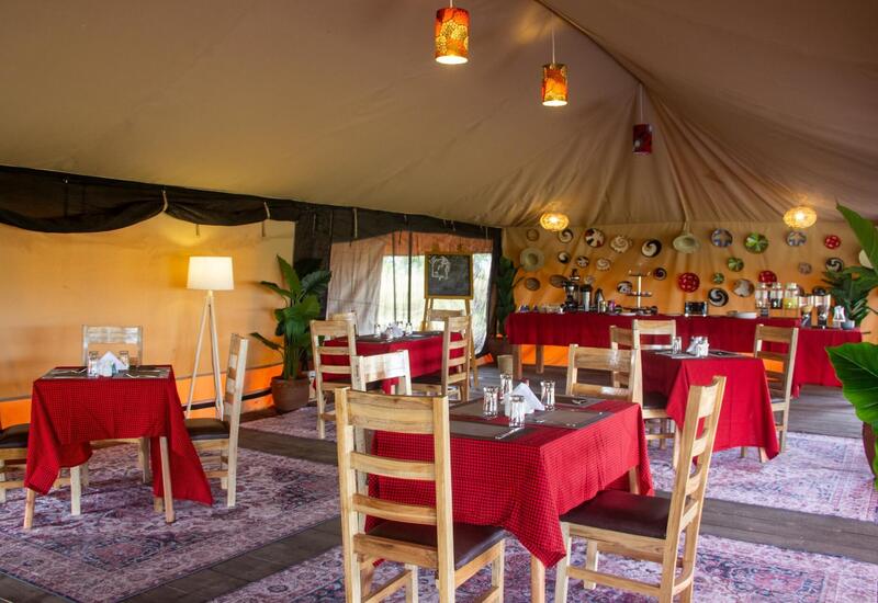 Tented safari dining room with wooden chairs, red-checked tables, buffet station, warm pendant lights and decorative wall plates.