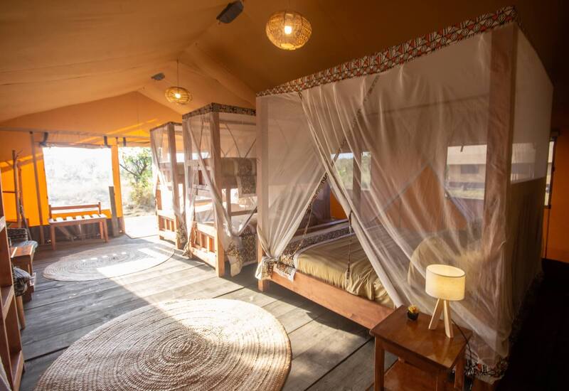 Spacious safari-style tent with two mosquito-netted wooden beds, woven rugs, warm lanterns and open porch views of bush.