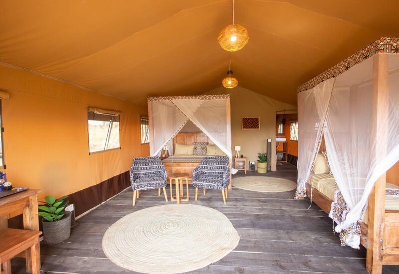 Safari tent suite with wooden floors, two mosquito‑net beds, patterned armchairs, woven rugs and rattan lights