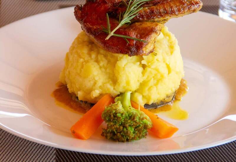 Mashed potatoes topped with roasted chicken wing and rosemary, served with carrots, broccoli and a savory jus.