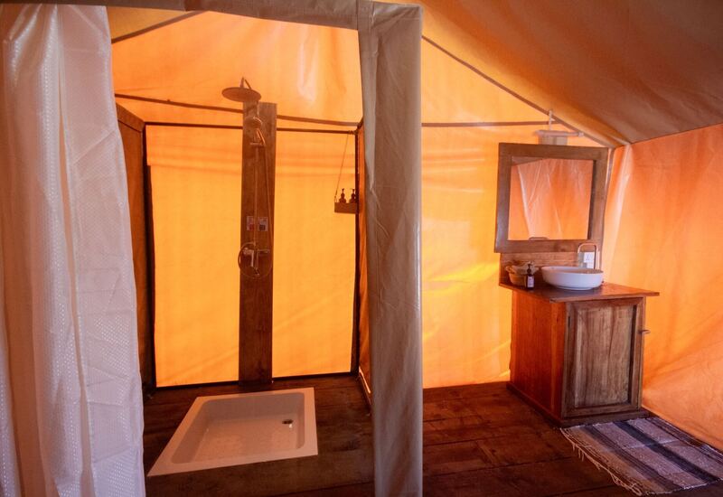 Glamping tent bathroom with rain shower on wooden post, shower tray, rustic wooden vanity, vessel sink and mirror