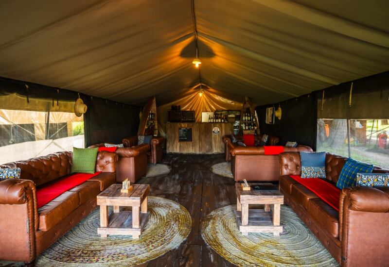Glamping lounge tent with leather sofas, colorful cushions, rustic wooden tables, woven rugs and a small bar.