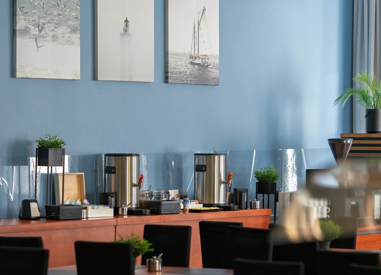 Jadalnia hotelowa z bufetem śniadaniowym, stalowymi podgrzewaczami kawy, drewnianymi stołami, czarnymi krzesłami i morskimi obrazami na niebieskiej ścianie