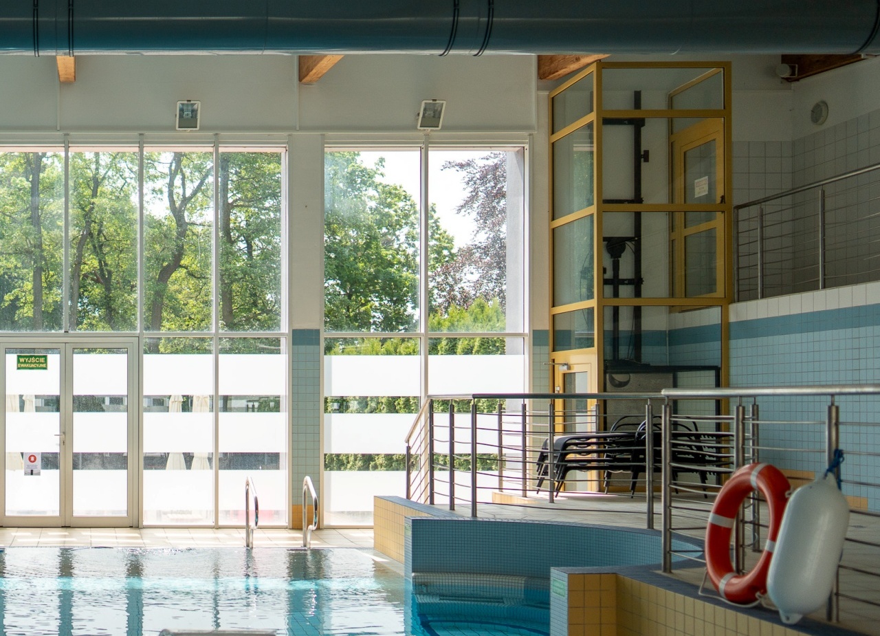 Kryty basen hotelowy z dużymi oknami na zieleń, kaskadą wodną, barierkami, leżakami i kołem ratunkowym